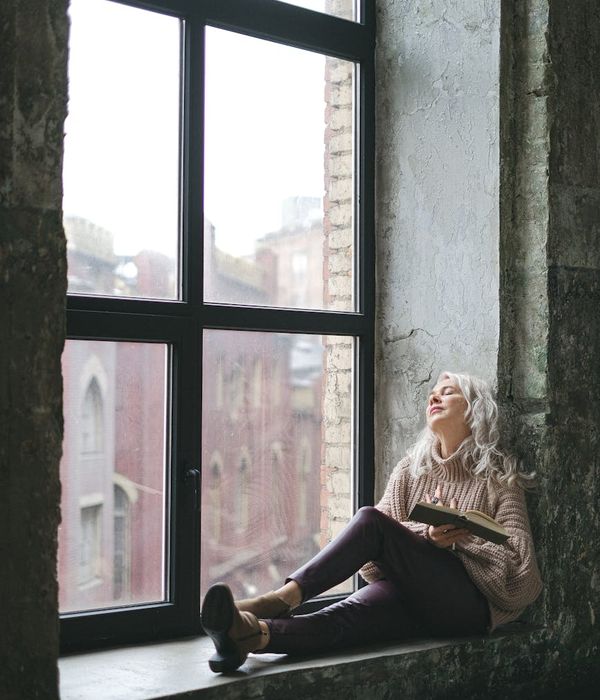 A serene person sitting calmly by a large window.